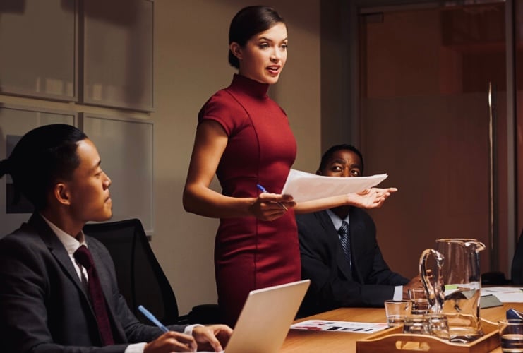 A businesswoman holding a pen and paper, and speaking in a meeting